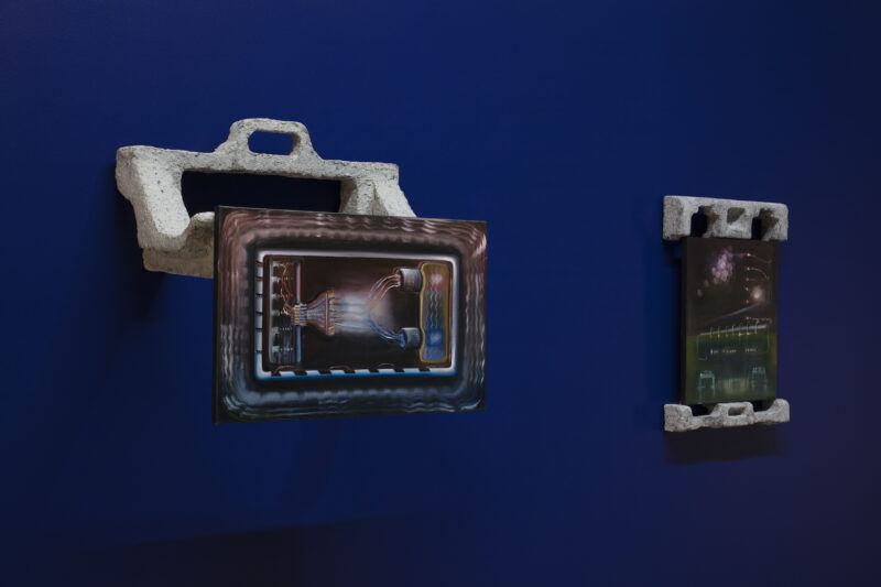 Two abstract artworks mounted on a deep blue wall, each framed by a gray, textured material resembling concrete.