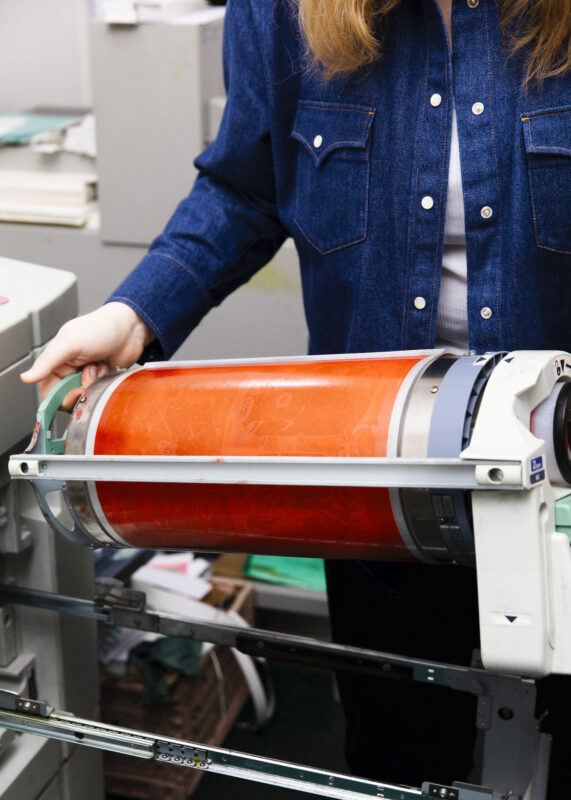 Hands holding a risograph orange ink drum.