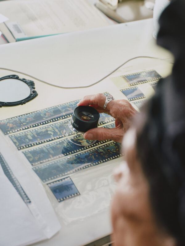 Alanis Obomsawin examines photographic film negatives on a light table using a magnifier.