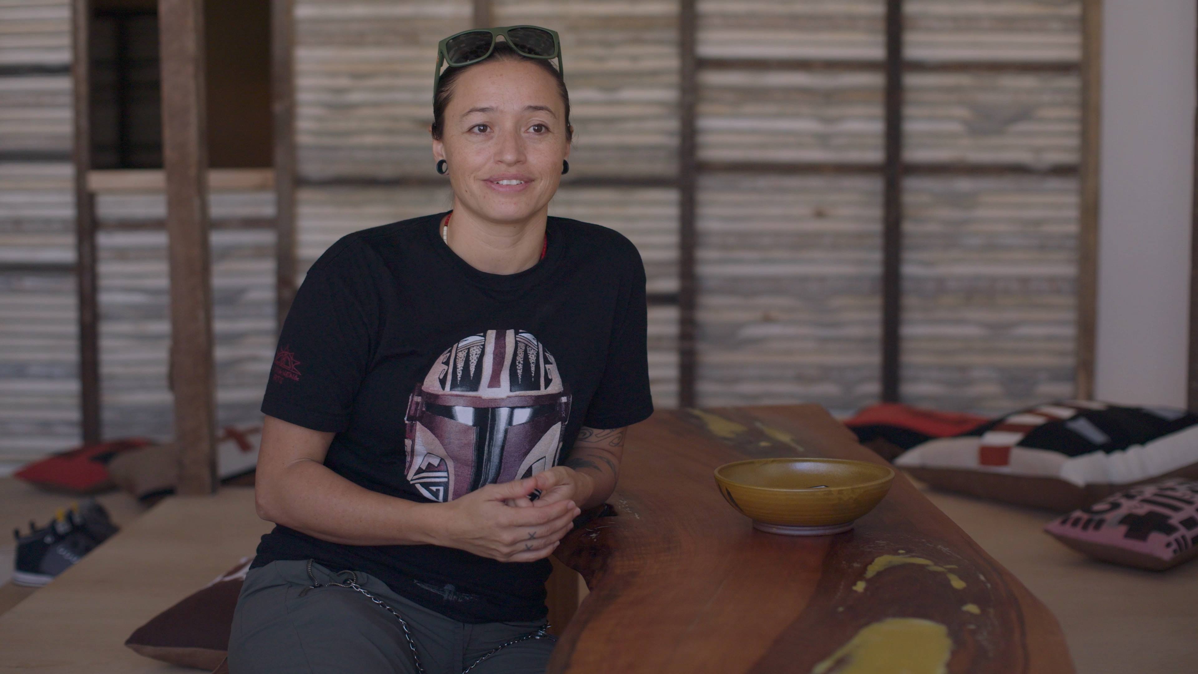 Rose B. Simpson hands clasped sitting in front of the wooden walls of her installation, "Dream House."