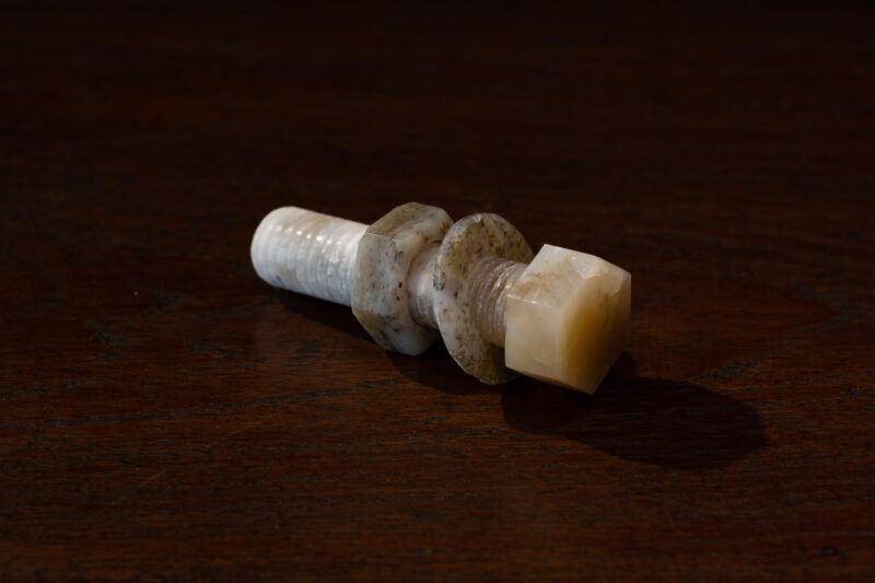 A sculpture resembling a bolt made of Nephrite lies on a dark wooden surface.