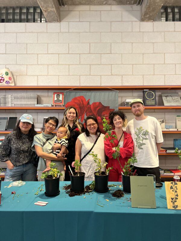 Group of Atomic Terrain members standing in front of a blue clothe covered table with four plants in black pots.