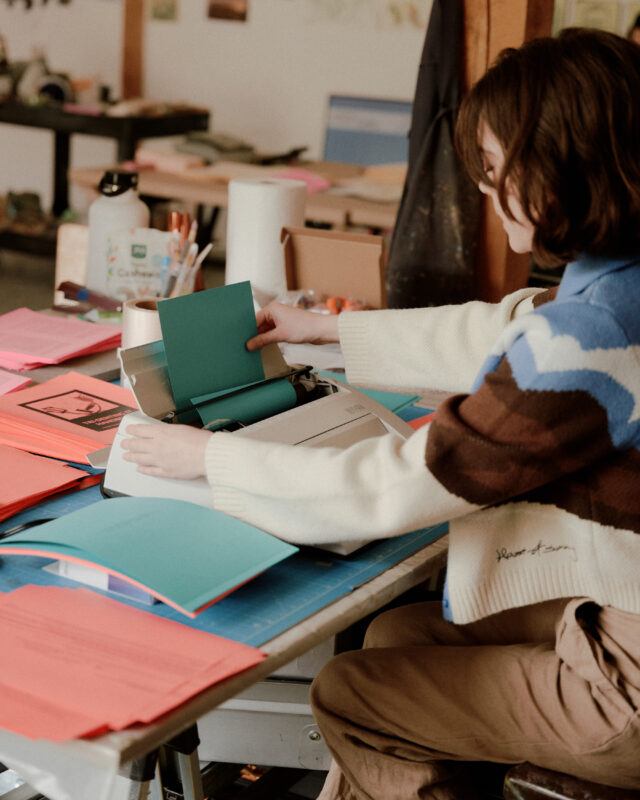 Daniella Porras inserting a blue sheet of paper into a typewriter.