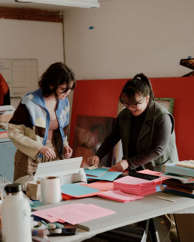 Daniella Porras and Tammy Nguyen working over a table with bright pink and blue papers.