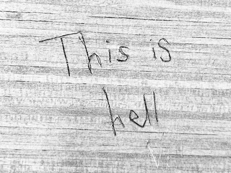 "This is hell" carved into a textured wall.